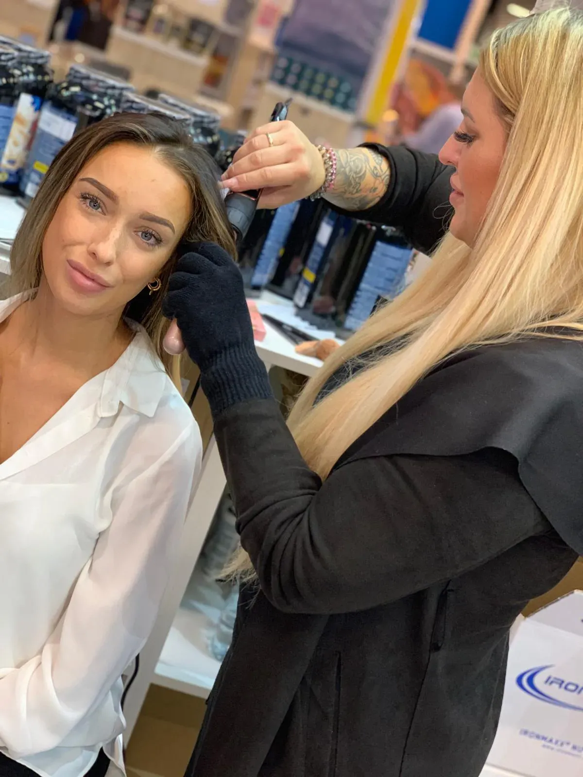 Ein Stylist lockt einer Frau in einem Salon oder bei einer Schönheitsveranstaltung mit einem Lockenstab die Haare.