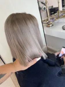 Person mit glattem, kinnlangem aschblondem Haar, von hinten gesehen, hält ein Telefon.