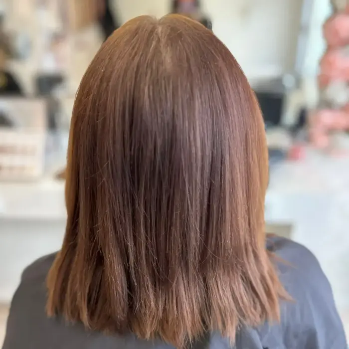 Person mit glattem, schulterlangem braunem Haar, von hinten gesehen in einem Salon.